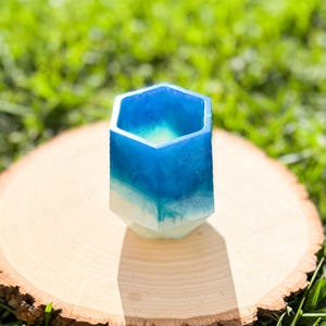 May include: A hexagonal shaped planter made of resin with a white and blue ombre design. The planter is sitting on a wooden surface.