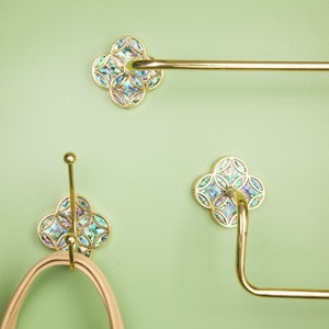 May include: Gold bathroom hardware set with iridescent shell accents. The set includes a towel bar, a double hook, and a toilet paper holder.