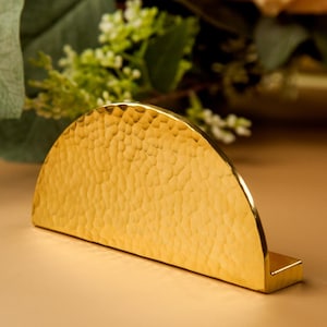 Puede incluir: Un tirador de armario de media luna dorado con textura martillada.