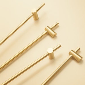 May include: Four gold-toned metal cabinet pulls with a simple, straight design. Each pull has a round knob on one end and a straight bar extending from the knob.