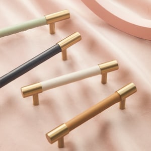 Puede incluir: Cuatro tiradores de armario con bases de metal dorado y tapas de diferentes colores. Los tiradores están dispuestos en fila sobre una superficie rosa. Los colores de los tiradores son verde claro, azul oscuro, blanco y marrón.