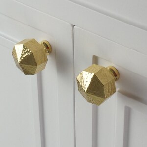May include: Two gold-toned cabinet knobs with a hammered finish and a geometric shape.