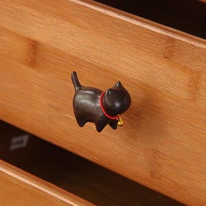 May include: A wooden black cat drawer pull with a red collar and a gold bell.