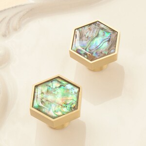 May include: Two hexagonal cabinet knobs with a gold finish and iridescent abalone shell inlays.