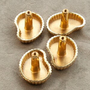 May include: Four gold-coloured cabinet knobs with a scalloped edge and a unique, organic shape. The knobs are designed to resemble a leaf or a teardrop.