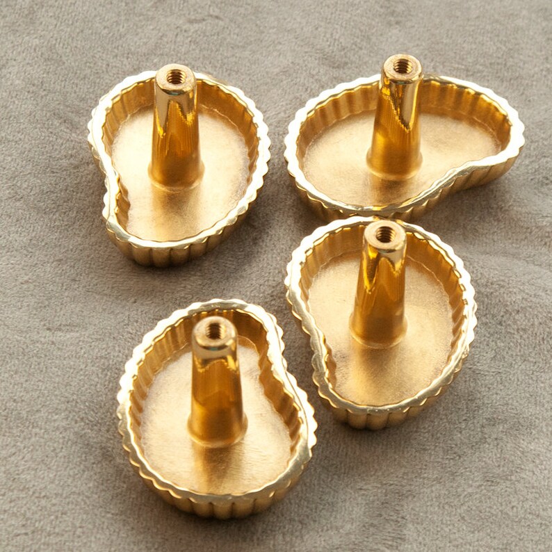 May include: Four gold-coloured cabinet knobs with a scalloped edge and a unique, organic shape. The knobs are designed to resemble a leaf or a teardrop.