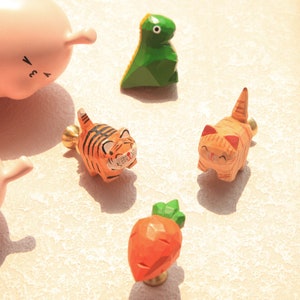 以下が含まれることがあります： 動物と野菜の形をした木製引き出しノブ5個。ノブは明るい色で塗られています。緑色の恐竜、オレンジ色の虎、オレンジ色の猫、ピンク色の豚、オレンジ色のニンジンがあります。