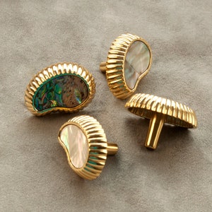 May include: Four gold-toned cabinet knobs with a decorative, ribbed design. Each knob features a different iridescent abalone shell inlay.
