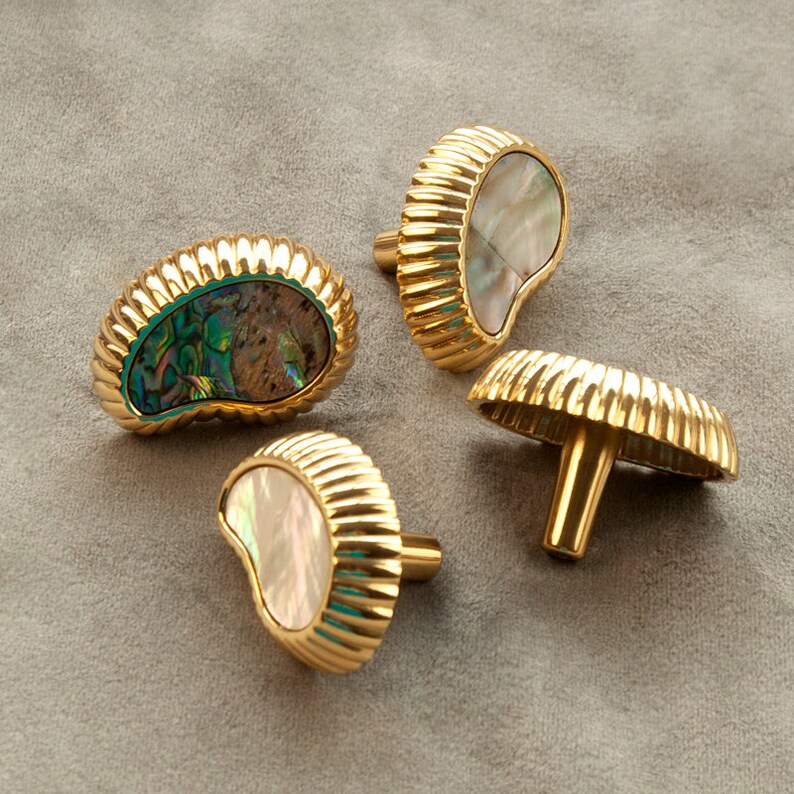 May include: Four gold-toned cabinet knobs with a decorative, ribbed design. Each knob features a different iridescent abalone shell inlay.
