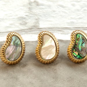 Op de afbeelding: Drie gouden oorbellen met een parelmoer abalone-schelp inlay. De oorbellen zijn traanvormig en hebben een getextureerde rand.