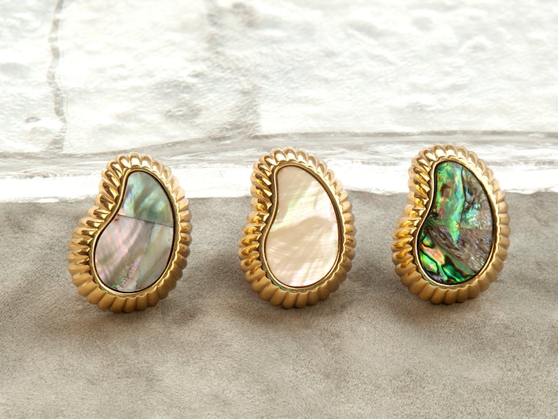 May include: Three gold-toned earrings with a pearlescent abalone shell inlay. The earrings are shaped like a teardrop and have a textured edge.
