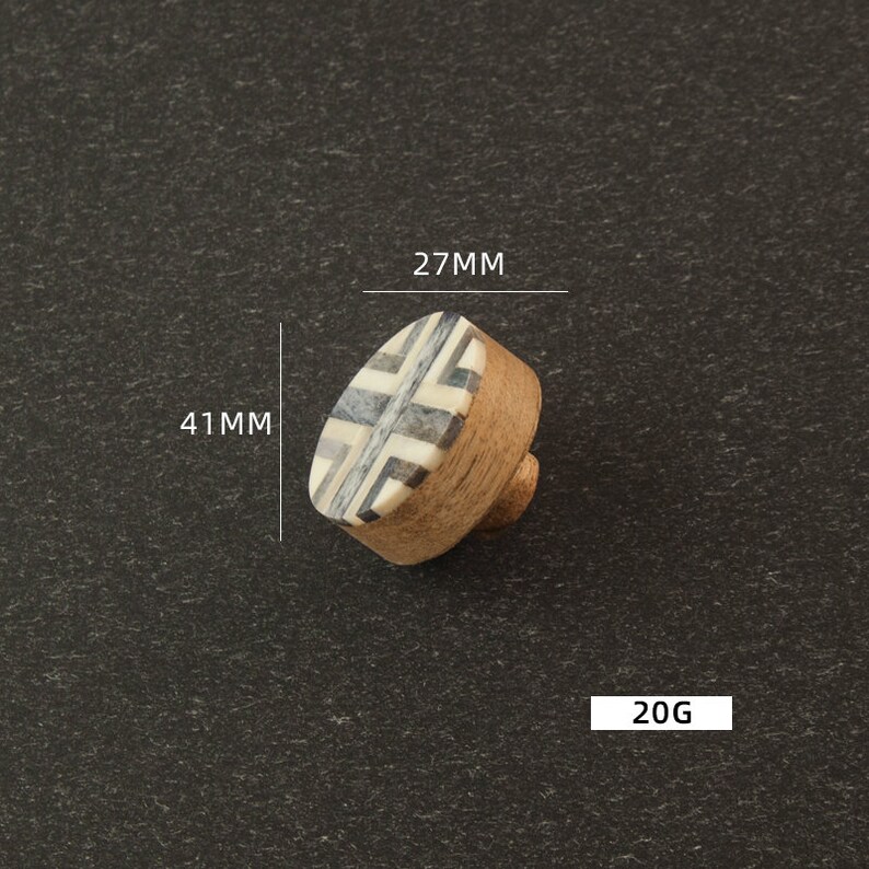 K&ouml;nnte beinhalten: Ein runder, h&ouml;lzerner Knopf mit einem schwarz-wei&szlig;en geometrischen Muster. Der Knopf hat einen Durchmesser von 27 mm und eine H&ouml;he von 41 mm. Er wiegt 20 Gramm.