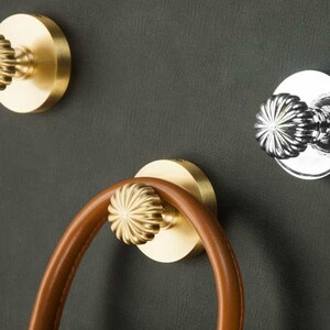May include: Three gold-toned wall hooks with a decorative, starburst-shaped knob. The hooks are mounted on a dark green wall.