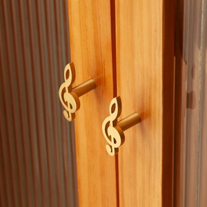 以下が含まれることがあります： 木製のキャビネットのドアに取り付けられた、トレブル・クレフの形をした金色のドアノブが2つあります。