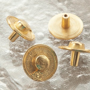 May include: Four gold-toned cabinet knobs with a decorative, textured, circular design resembling a hat. The knobs have a cylindrical stem.