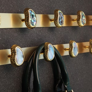 May include: Gold wall mounted hooks with iridescent shell-like knobs. A green leather handbag hangs on one of the hooks.