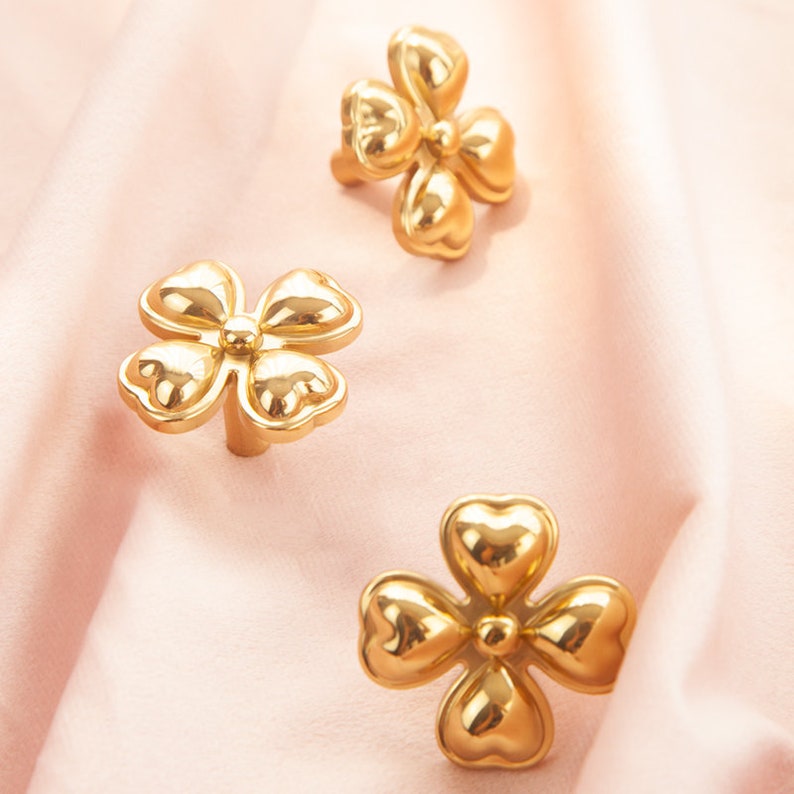 May include: Three gold-colored metal flower-shaped drawer pulls. Each pull has five petals and a raised center.