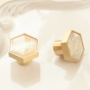 May include: Two gold hexagonal cabinet knobs with a white iridescent mother of pearl inlay.