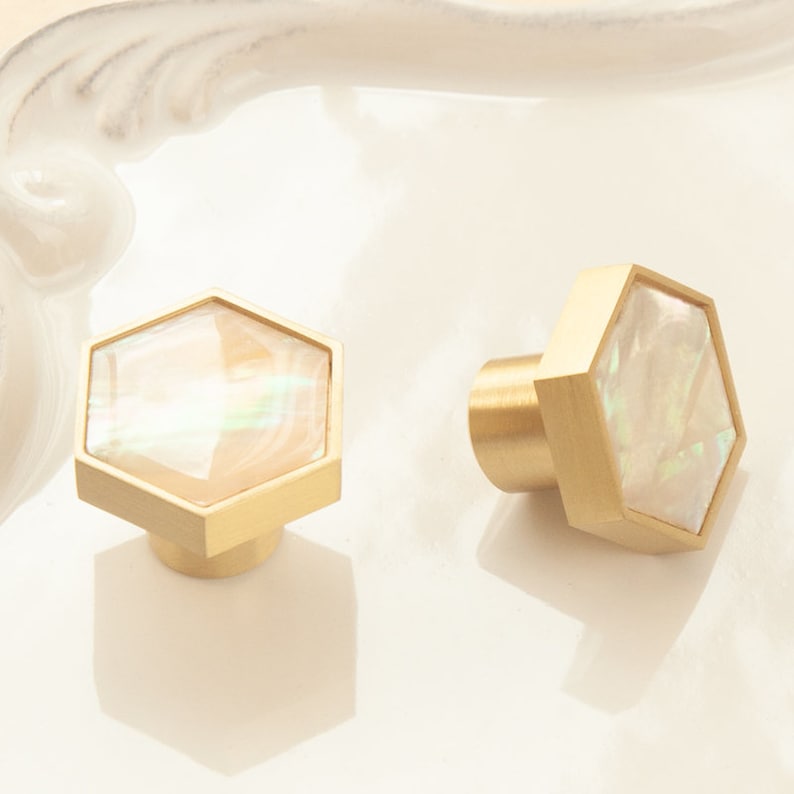 May include: Two gold hexagonal cabinet knobs with a white iridescent mother of pearl inlay.