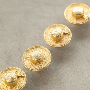 May include: Four gold-toned hat-shaped buttons with a textured surface. Each button has a small flower detail.