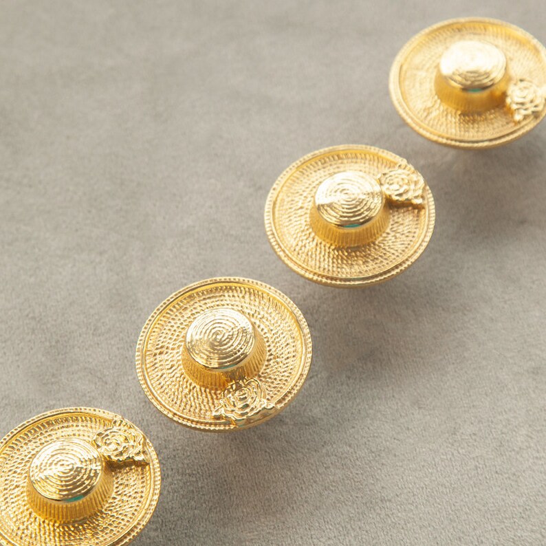 May include: Four gold-toned hat-shaped buttons with a textured surface. Each button has a small flower detail.