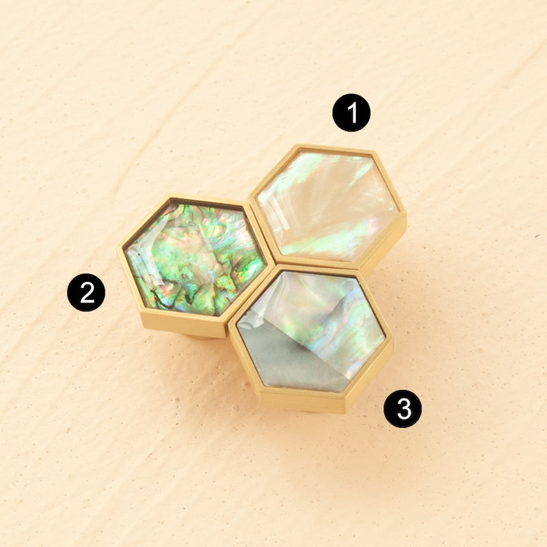 May include: Three hexagonal cabinet knobs with a gold finish and iridescent mother-of-pearl inlays. The knobs are arranged in a cluster.