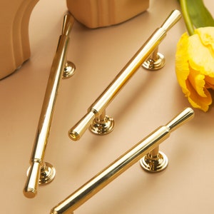 Op de afbeelding: Drie gouden kastgrepen met een cilindrisch ontwerp. De grepen hebben een gladde, gepolijste afwerking.