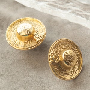 May include: A pair of gold-tone earrings shaped like straw hats with a small flower detail.