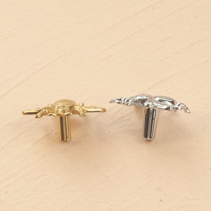 Peut inclure: Deux boutons d&eacute;coratifs pour armoire en forme de scorpion stylis&eacute;. Le bouton de gauche est dor&eacute; et le bouton de droite est argent&eacute;.