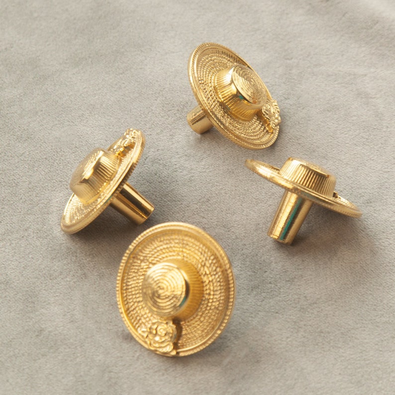 May include: Four gold-toned cabinet knobs shaped like straw hats with a floral design. The knobs have a threaded post for attaching to a cabinet door.