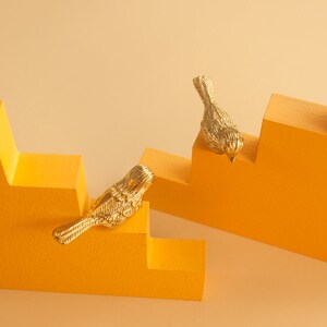 May include: Two gold bird figurines perched on a set of yellow steps. The steps are made of wood and have a textured surface.