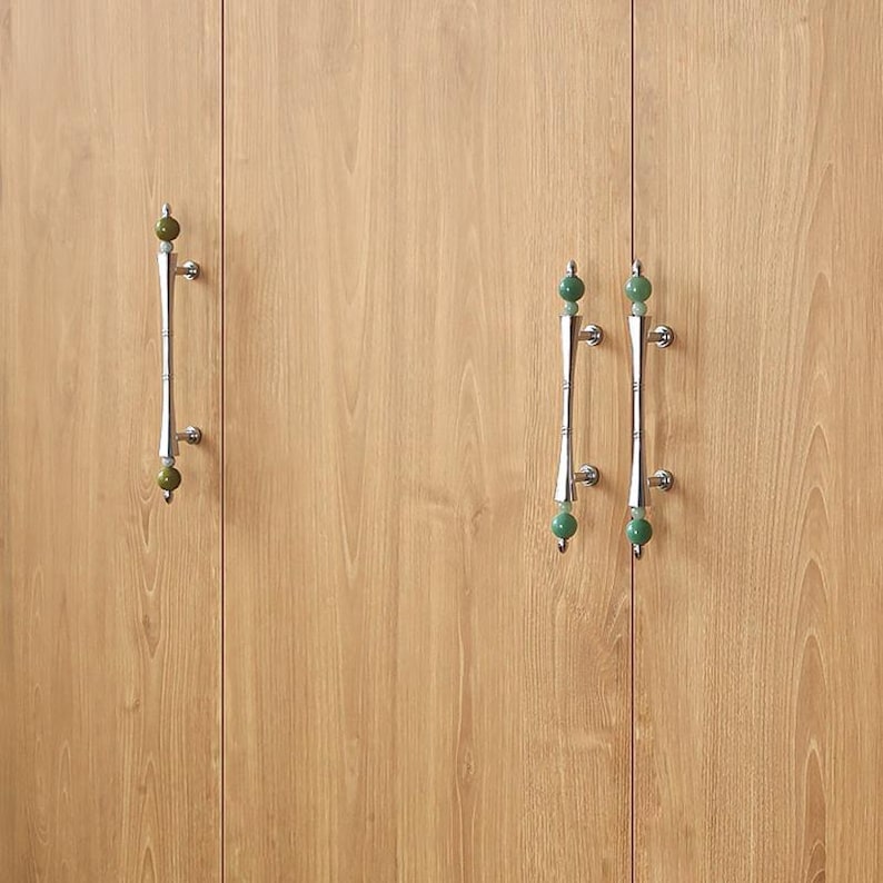 Puede incluir: Tiradores de puerta de armario con asas plateadas y detalles esf&eacute;ricos verdes. Los tiradores est&aacute;n montados en un armario de madera marr&oacute;n claro. Los tiradores tienen un dise&ntilde;o similar al bamb&uacute;.