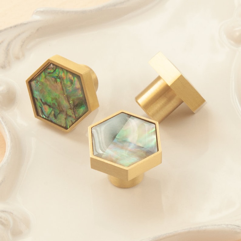 May include: Three hexagonal cabinet knobs with a brass finish and iridescent abalone shell inlays.