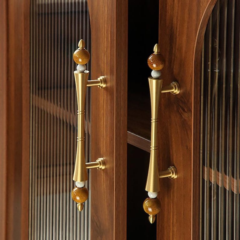 Op de afbeelding: Close-up van een houten kast met twee deuren. Elke deur heeft een messing handvat met een decoratieve, bolvormige bovenkant. De kastdeuren zijn donkerbruin en de glazen panelen hebben verticale lijnen.