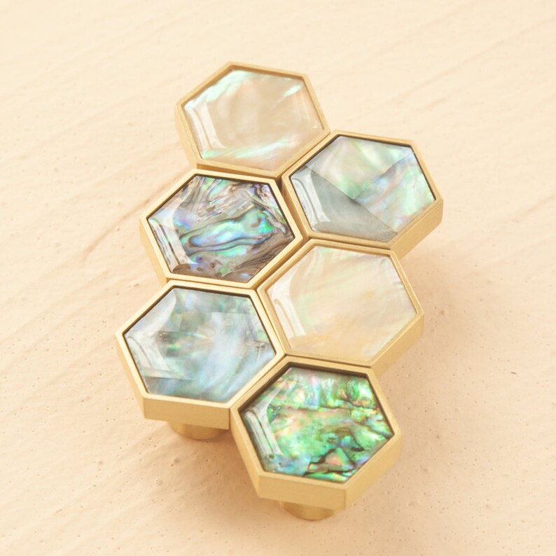May include: A set of six hexagonal cabinet knobs with a gold finish and iridescent mother-of-pearl inlays. The knobs are arranged in a honeycomb pattern.