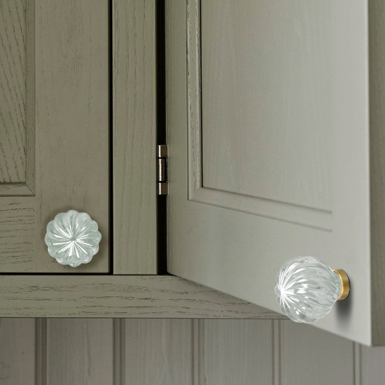 May include: Two clear glass cabinet knobs with a textured, fluted design. The knobs have a gold metal base.