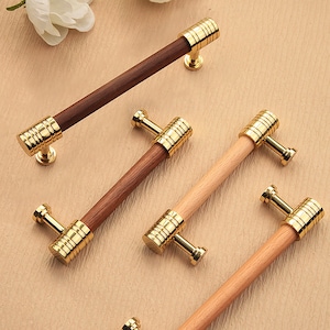 Puede incluir: Cuatro tiradores de armario con acabado dorado y manijas de madera. Dos tiradores tienen una manija de madera clara y dos tiradores tienen una manija de madera oscura.