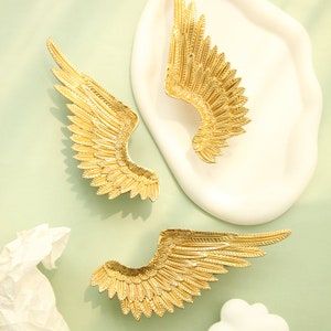 May include: A pair of gold-tone angel wing earrings. The wings are detailed with a textured feather design.