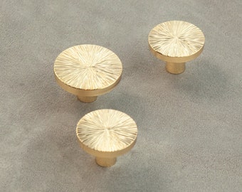 May include: Three gold-toned round cabinet knobs with a textured, sunburst design. The knobs have a short, cylindrical base.