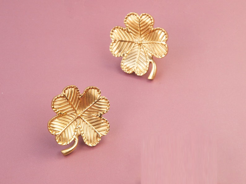 Peut inclure: Une paire de boucles d'oreilles en forme de tr&egrave;fle &agrave; quatre feuilles de couleur dor&eacute;e. Les boucles d'oreilles sont en m&eacute;tal et ont une surface textur&eacute;e.