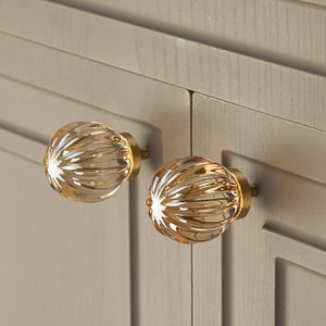 May include: Two amber glass cabinet knobs with a fluted design and gold metal hardware.