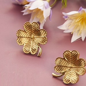 Peut inclure: Une paire de boucles d'oreilles en forme de tr&egrave;fle &agrave; quatre feuilles dor&eacute;es. Les boucles d'oreilles sont en m&eacute;tal et pr&eacute;sentent un design d&eacute;taill&eacute;.