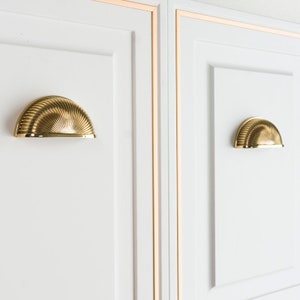 May include: Two white cabinet doors with gold trim and gold cup-shaped cabinet pulls.