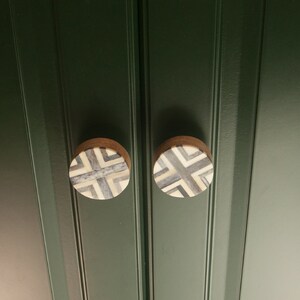 K&ouml;nnte beinhalten: Zwei runde, h&ouml;lzerne Schrankkn&ouml;pfe mit einem geometrischen Muster aus schwarzen und wei&szlig;en Streifen. Die Kn&ouml;pfe sind an einer dunkelgr&uuml;nen Schrankt&uuml;r montiert.