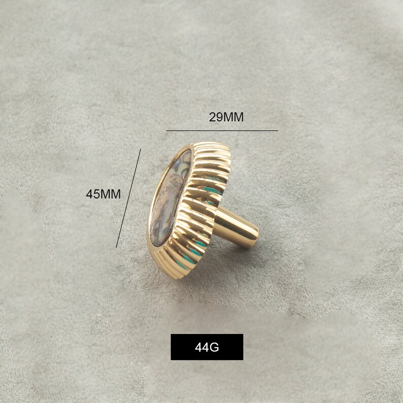 May include: A gold-toned cabinet knob with a decorative, oval-shaped shell inlay. The knob measures 29 mm in diameter and 45 mm in height. It weighs 44 grams.