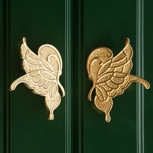 Puede incluir: Dos tiradores de puerta de mariposa dorados con detalles intrincados.