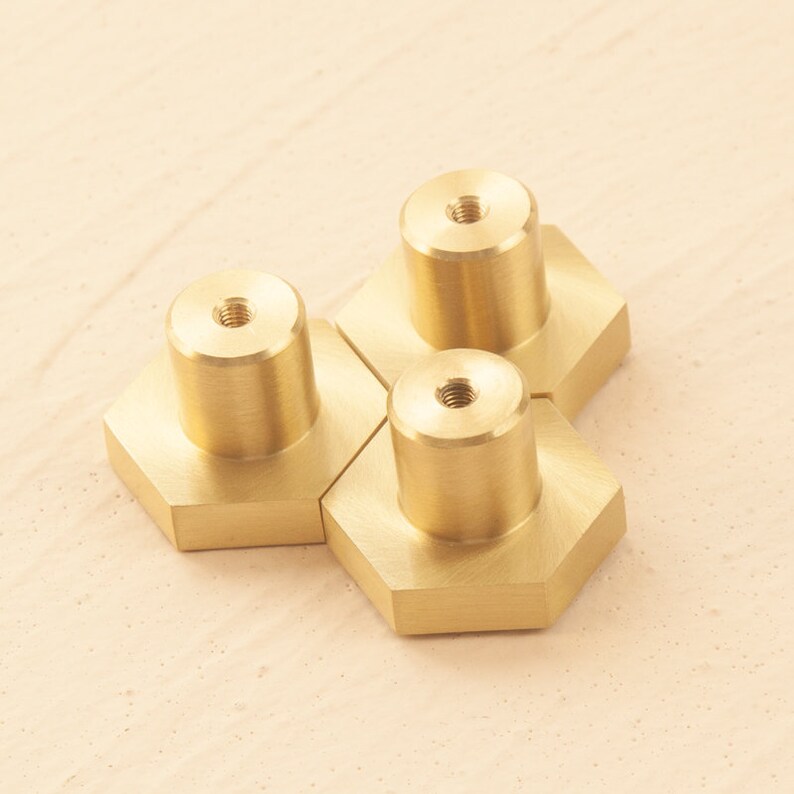 May include: Three gold hexagonal cabinet knobs with a screw hole in the center of each knob.