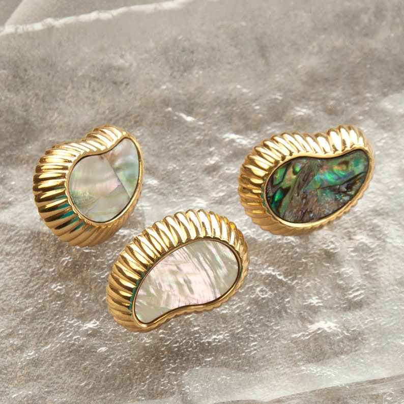 May include: Three gold-toned, shell-shaped earrings with iridescent abalone inlay. The earrings are in the shape of a teardrop with a ribbed edge.