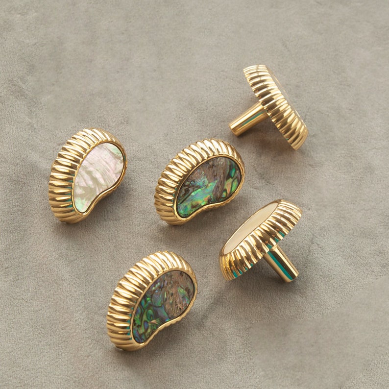 May include: Five gold cabinet knobs with a mother of pearl inlay. The knobs are in the shape of a half-moon or crescent.