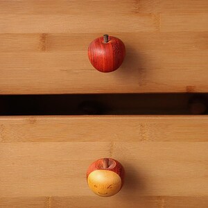 May include: Two wooden drawer pulls shaped like apples. The top pull is red and the bottom pull is yellow with a smiley face.